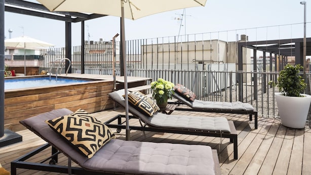 A rooftop terrace with a swimming pool, lounge chairs, and a large umbrella.