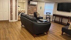 Een woonkamer met een zwarte leren bank, een houten salontafel, een televisie en een bakstenen muur.