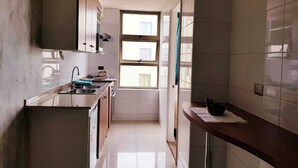 Eine schmale Küche mit Fenster, weißen Fliesenwänden und einer Arbeitsplatte mit Spüle und Herd.