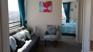 Ein Zimmer mit einer Couch, einem Sessel, einem Gemälde und Blick auf die Stadt durch ein Fenster.