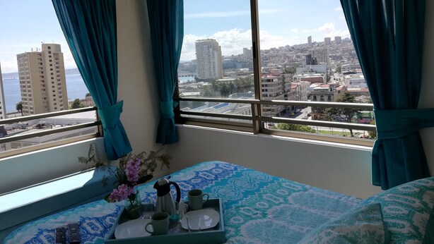 Ein Hotelzimmer mit Bett, Tablett mit Kaffee und Tee sowie Blick auf eine Stadtlandschaft.
