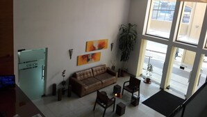 Eine geräumige Lobby mit einem braunen Ledersofa, einem Couchtisch und einer Topfpflanze. Links befindet sich ein Kühlschrank und rechts ein großes Fenster.