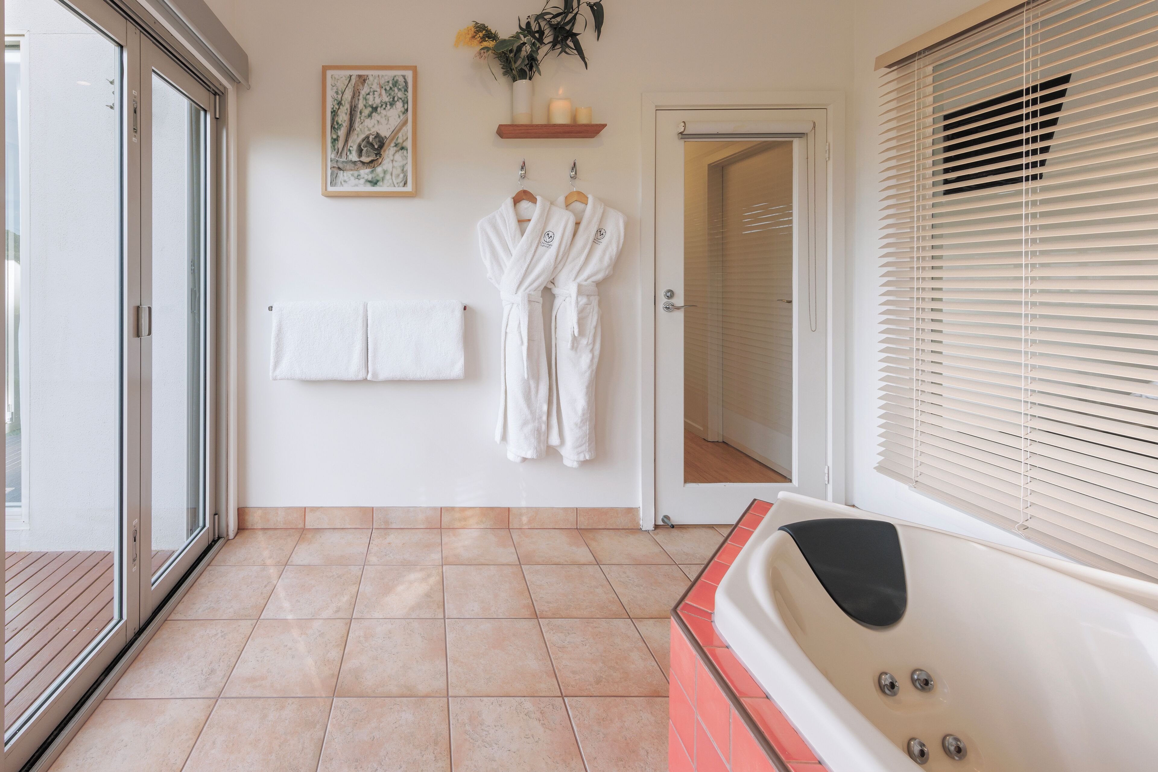 Un baño con bañera, un perchero con toallas y una puerta que da a otra habitación.