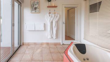 Un baño con bañera, un perchero con toallas y una puerta que da a otra habitación.
