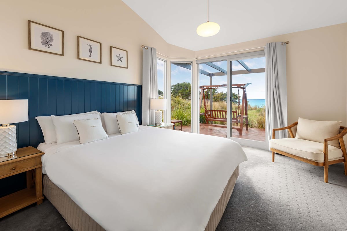 A spacious bedroom with a large bed, a wooden nightstand, a chair, and a view of the outdoors through a sliding glass door.