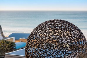 Een bolvormige metalen sculptuur met een geometrisch patroon, uitkijkend over een kustgebied met gebouwen en uitzicht op zee.