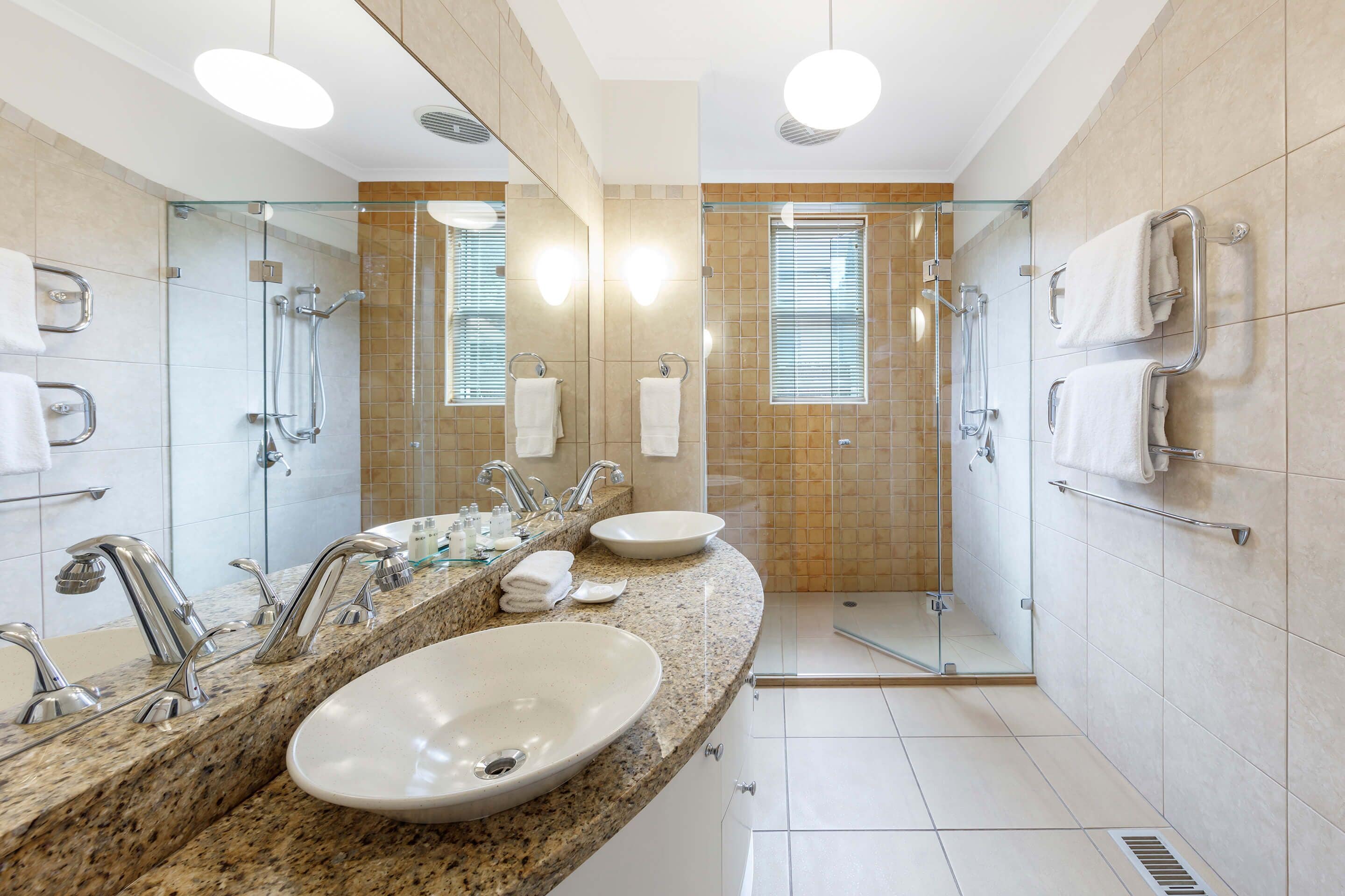 Une salle de bain moderne avec un comptoir en granit, deux vasques, une cabine de douche en verre et un grand miroir.