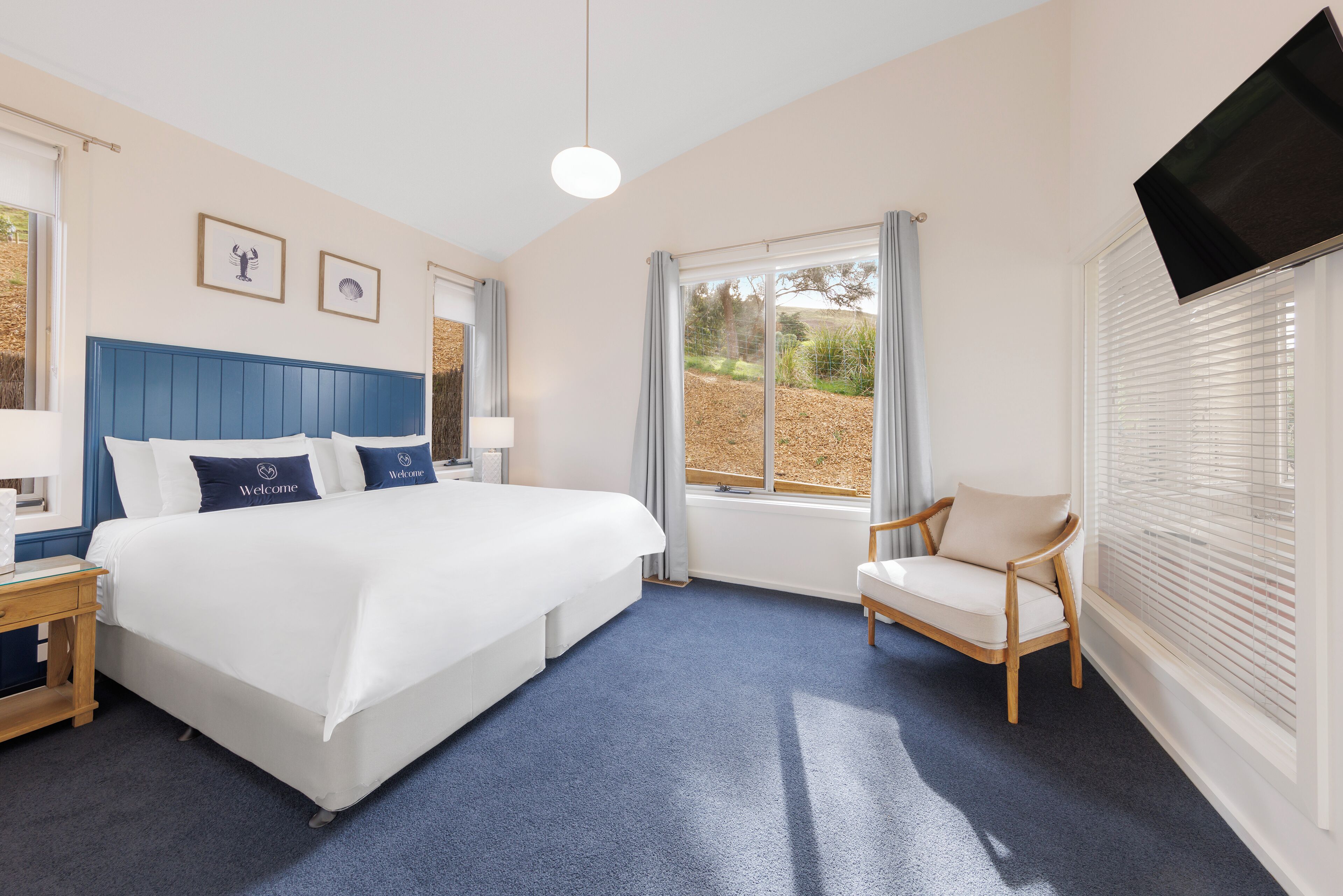 Ein Hotelzimmer mit einem großen Bett, einem Sessel, einem Fernseher und einem Fenster mit Jalousien.