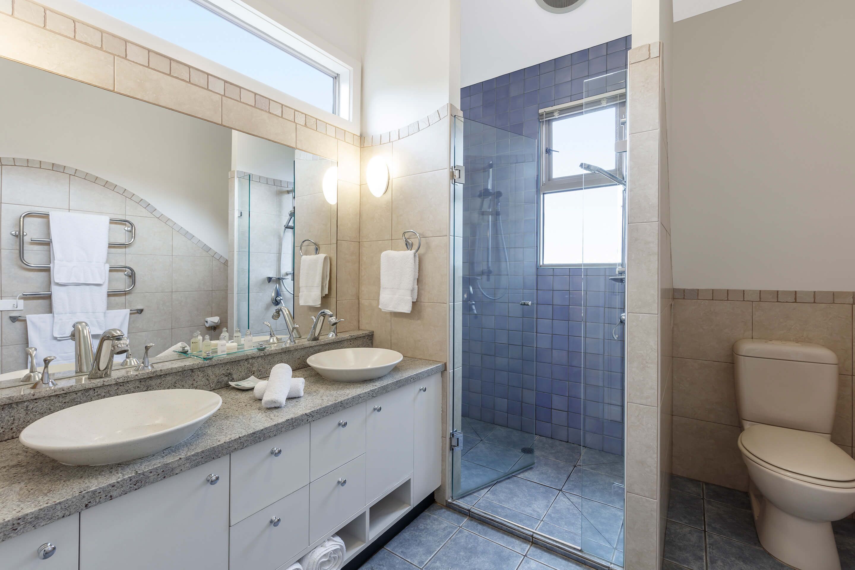 Un baño moderno con dos lavamanos, un espejo grande y una ducha con cerramiento de vidrio.