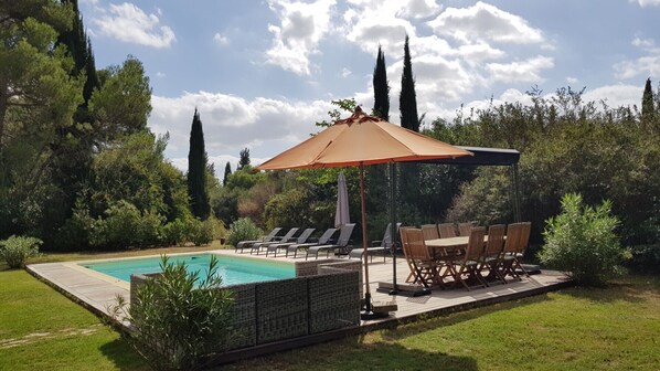 A backyard with a swimming pool, lounge chairs, a table, and a pergola with an umbrella.