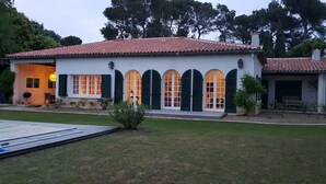 Une maison à deux étages, avec un toit recouvert de tuiles, des volets verts et un petit jardin devant.