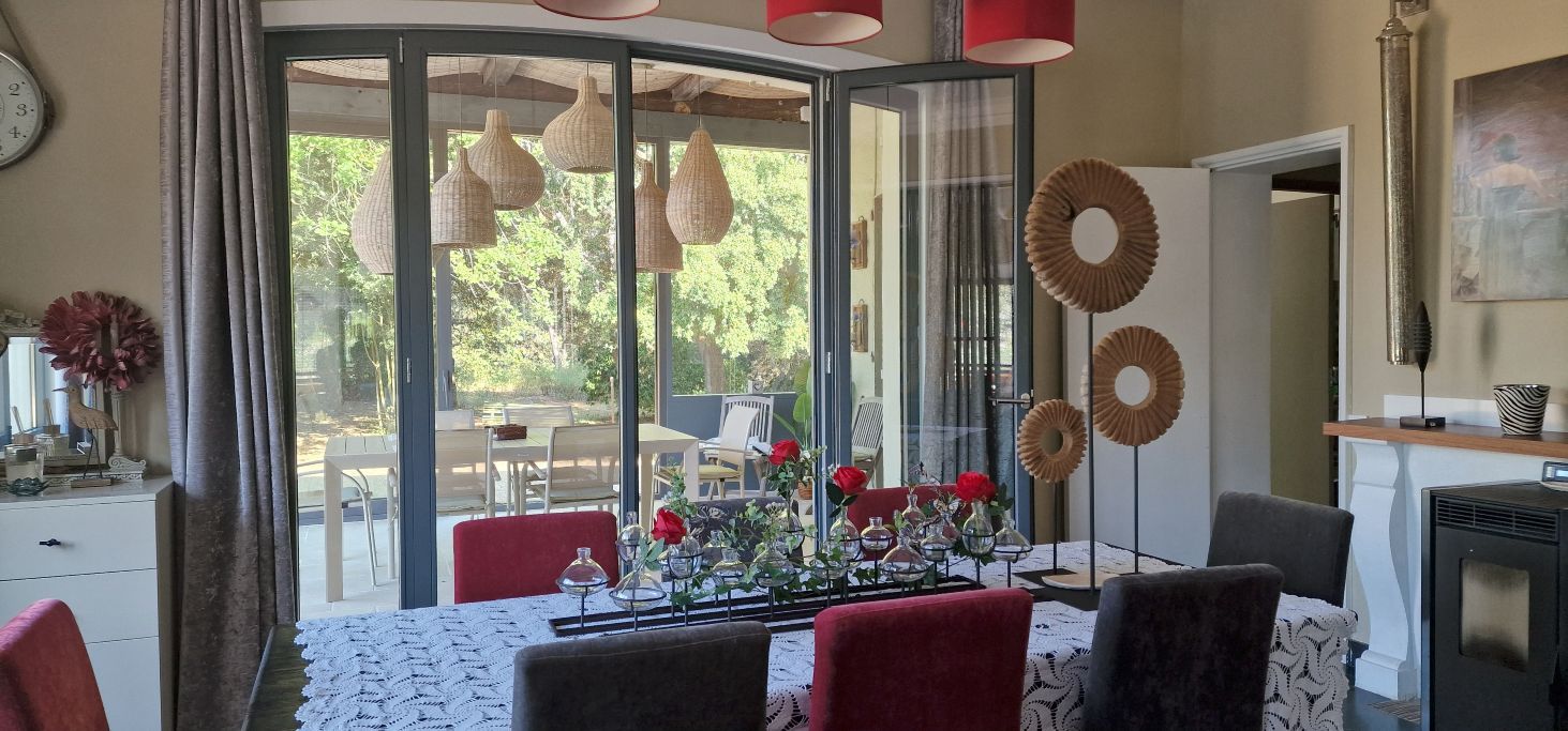A dining area with a glass partition, red chairs, a table set with a lace tablecloth, and hanging wicker lamps.
