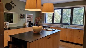 Une cuisine moderne dotée d’un grand îlot central, de meubles en bois et d’une fenêtre offrant une vue sur les arbres.