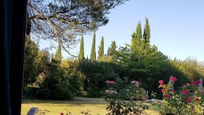 Une terrasse en bois avec deux chaises et un banc en bois, donnant sur un jardin où poussent différentes plantes et fleurs.