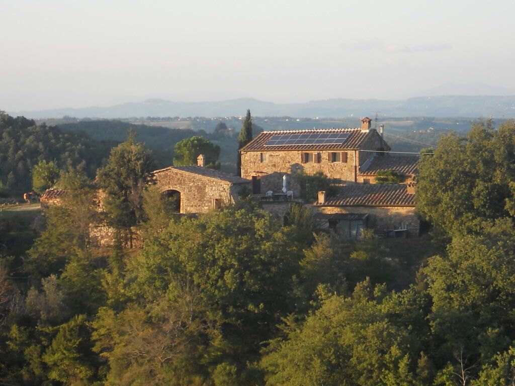Un edificio de piedra con techo de paneles solares, rodeado de árboles y colinas al fondo.