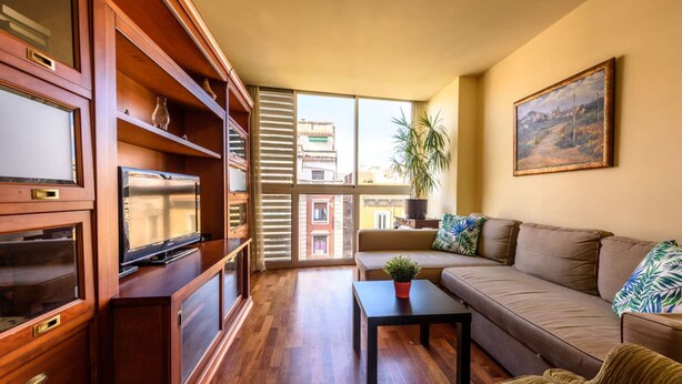 A spacious living room with a sofa, a coffee table, and a TV on a wooden cabinet. - Sepulveda - RamblasRentals Stylish Bright 3BR New Catalan Flat 10m Ramblas - Parking - Wifi (Barcelona)