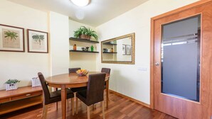 A dining area with a wooden table, four chairs, a bowl of fruit, and shelves with plants and decorative items. - Sepulveda - RamblasRentals Stylish Bright 3BR New Catalan Flat 10m Ramblas - Parking - Wifi (Barcelona)