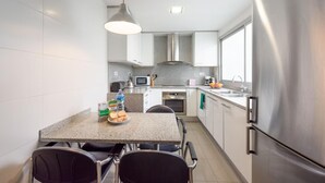 A modern kitchen with white cabinets, stainless steel appliances, a granite countertop, and a dining area with two chairs. - Sepulveda - RamblasRentals Stylish Bright 3BR New Catalan Flat 10m Ramblas - Parking - Wifi (Barcelona)