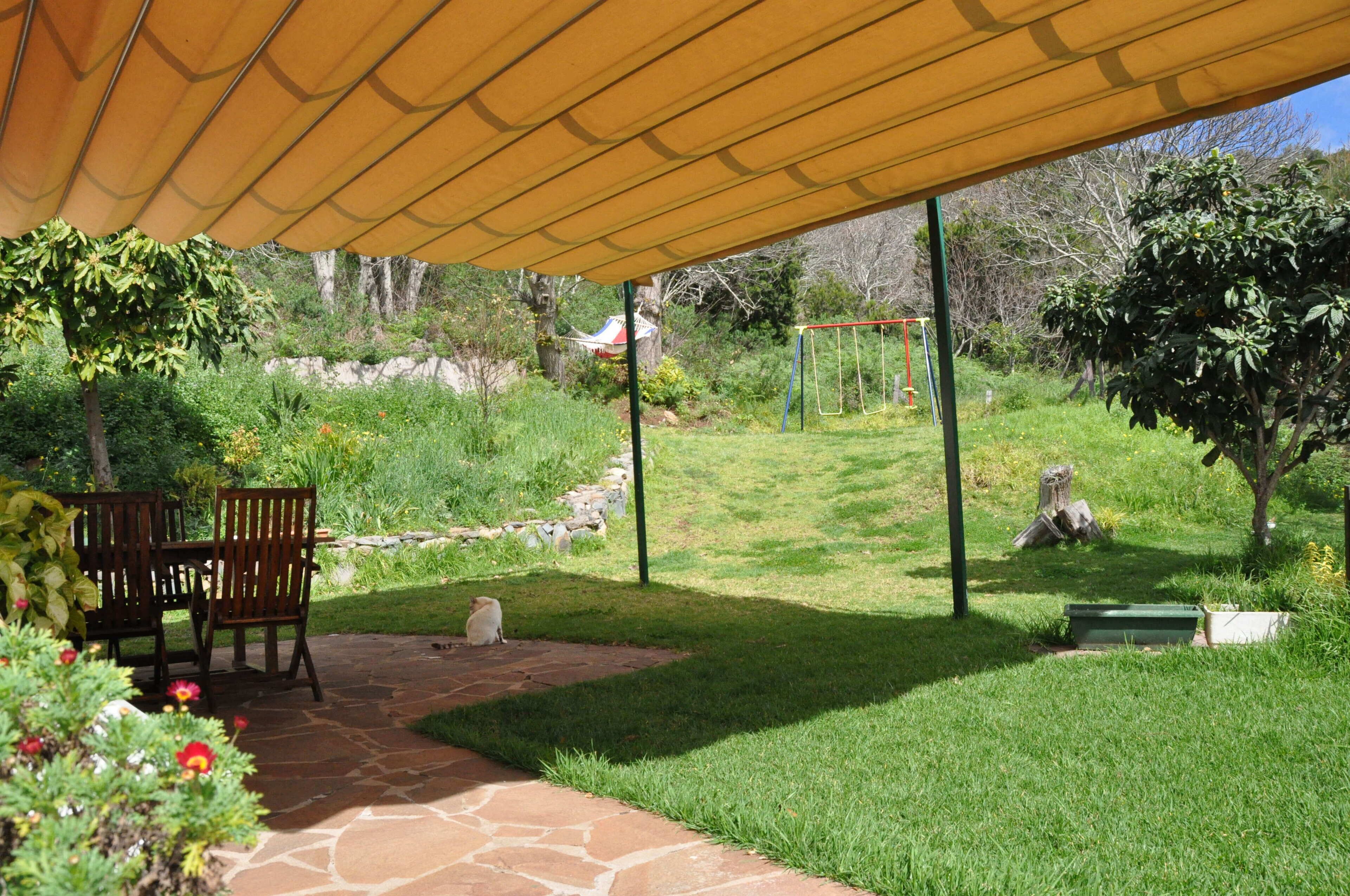 Une terrasse extérieure dotée d’un espace salon couvert, d’un chemin de pierre et d’une pelouse avec une balançoire.