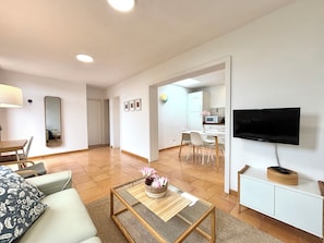 A modern living room with a sofa, coffee table, TV, and a kitchen area in the background.