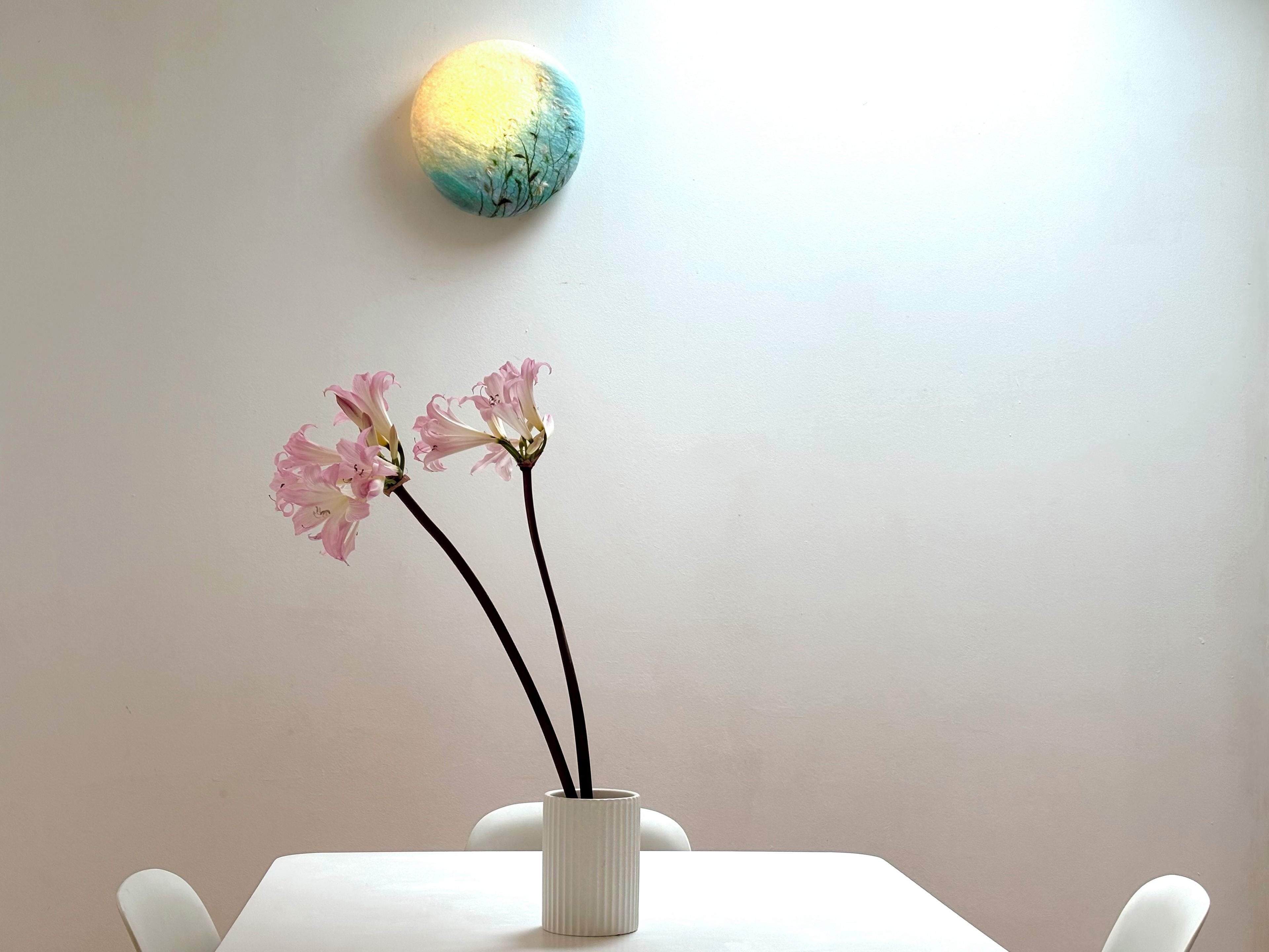 Ein weißer Tisch mit einer weißen Vase, die rosa Blumen und zwei schwarze Stiele enthält.