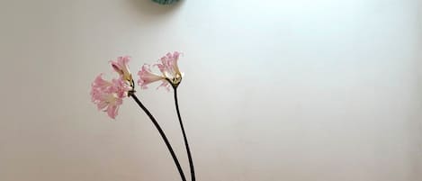 Una mesa blanca con un jarrón blanco que contiene flores rosadas y dos tallos negros.