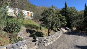 Un camí de pedra que condueix a un edifici blanc amb una porta de fusta, envoltat de vegetació i arbres.