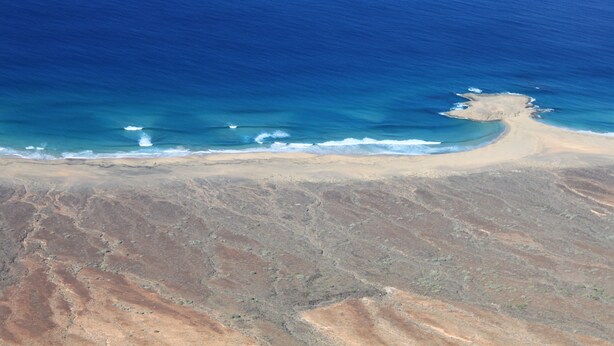 An aerial view of a beach with a sandy shoreline and a small island.