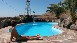 A child sitting by a pool with a waterfall feature.