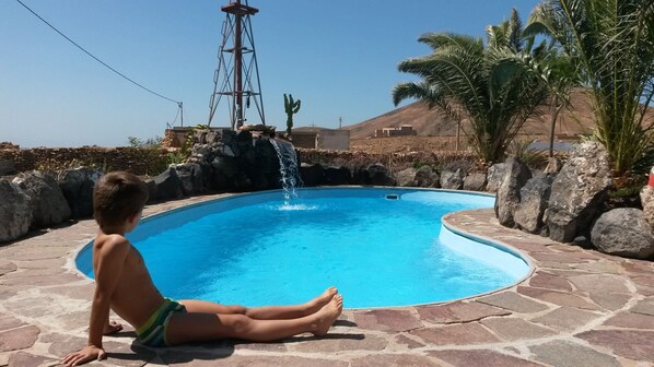 Un niño sentado junto a una piscina con una cascada.