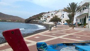 A coastal town with white buildings, a paved walkway, and a rocky shoreline.