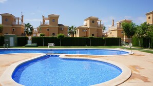 Una piscina de diseño curvo, rodeada por una zona pavimentada y un edificio con varios balcones y una antena parabólica.