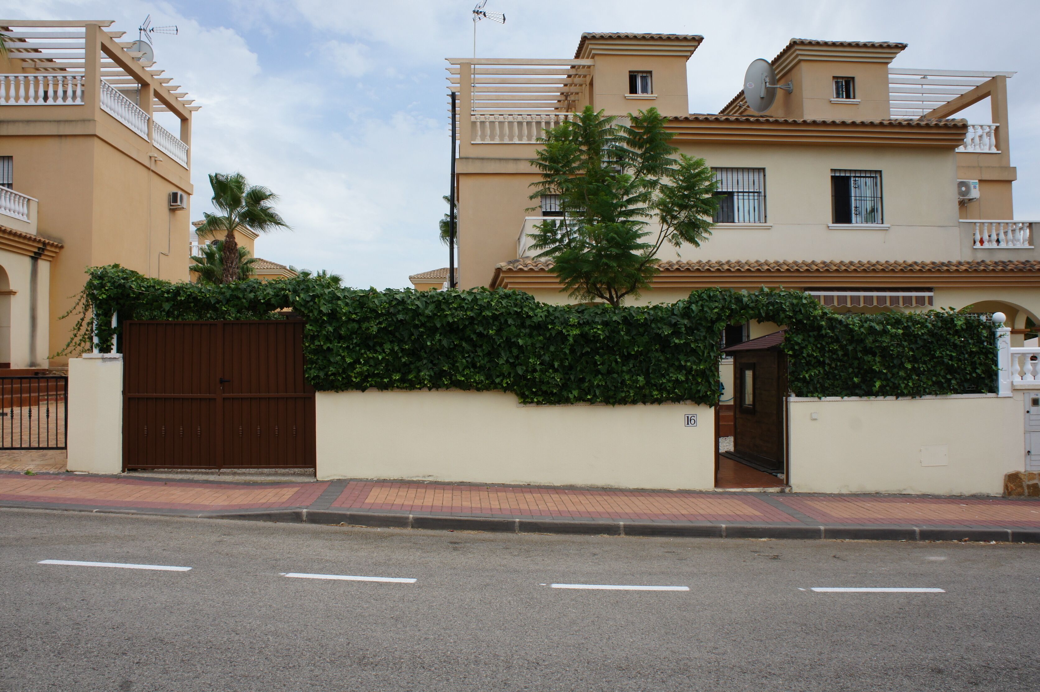 A residential building with a gated entrance, a paved sidewalk, and a clear sky.