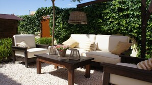 Un patio al aire libre con un sofá blanco, dos sillones, una mesa de centro de madera y una lámpara colgante de mimbre.