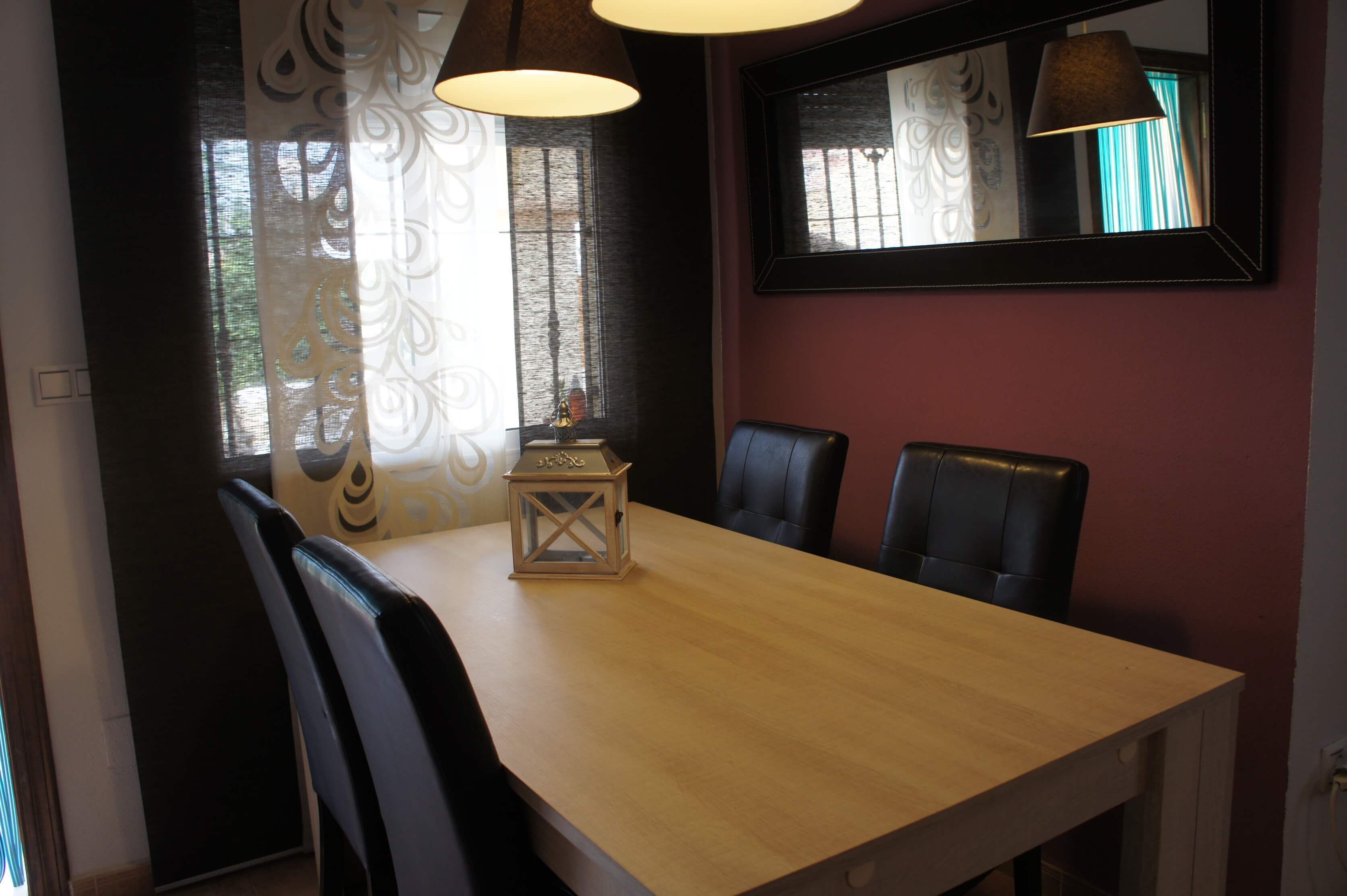 Un coin repas avec une table en bois, des chaises en cuir noir et une lanterne décorative.