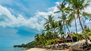 A beach with palm trees, a stone wall, and a building with a red roof.