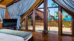 A bedroom with a TV, a bed, and large windows overlooking a pool area.
