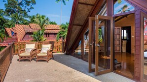 A resort with a thatched roof structure, wicker furniture, and a view of palm trees.