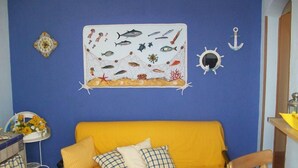 A room with a blue wall, a yellow sofa, and a wall hanging depicting marine life. - Apartment/ flat - Levanzo (Levanzo)