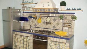 A compact kitchen with a gas stove, sink, and a refrigerator. There are hanging utensils and a potted plant on the wall. - Apartment/ flat - Levanzo (Levanzo)