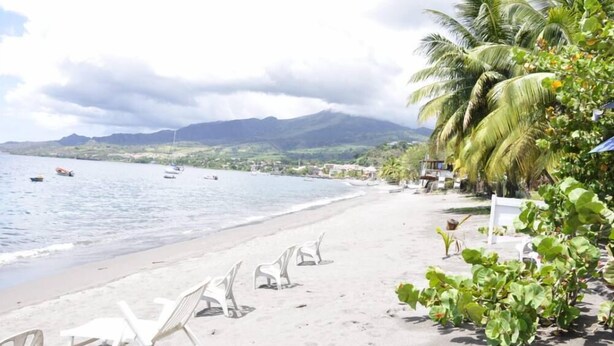 Une plage avec des chaises longues blanches et une vue sur la mer et les montagnes.