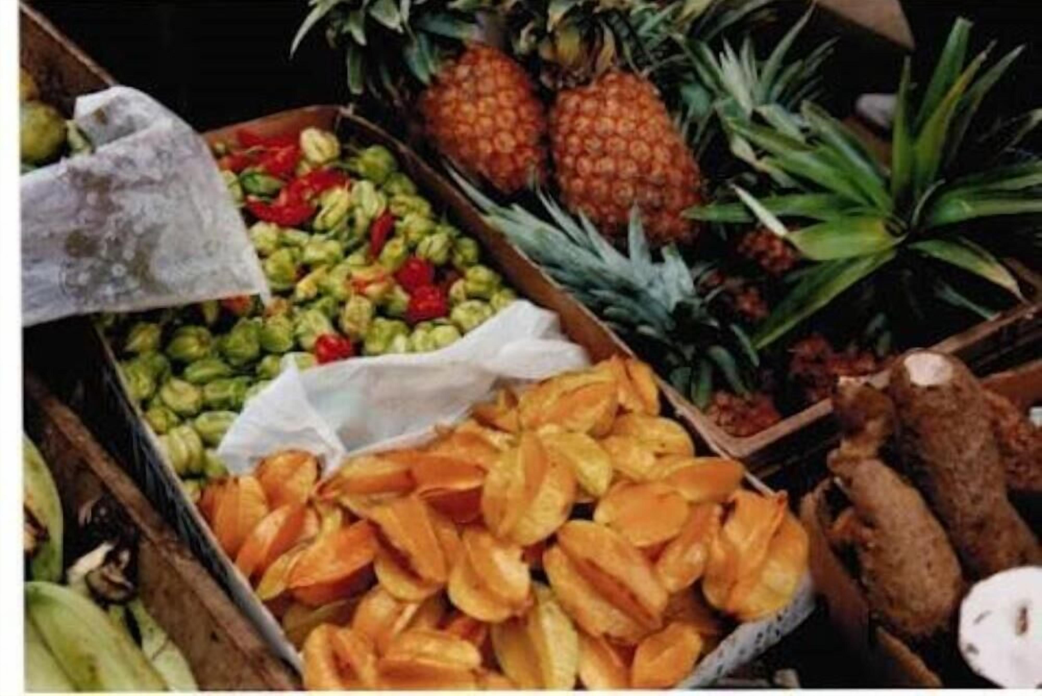 Une variété de fruits, notamment des ananas, des bananes et des papayes, présentés dans des caisses en bois.