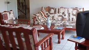 Un salon avec un canapé, des chaises en bois, une table basse et un téléviseur.