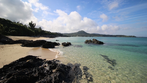A beach with clear turquoise water, rocky shoreline, and a distant mountain. - Akizero Onnason (Onna)