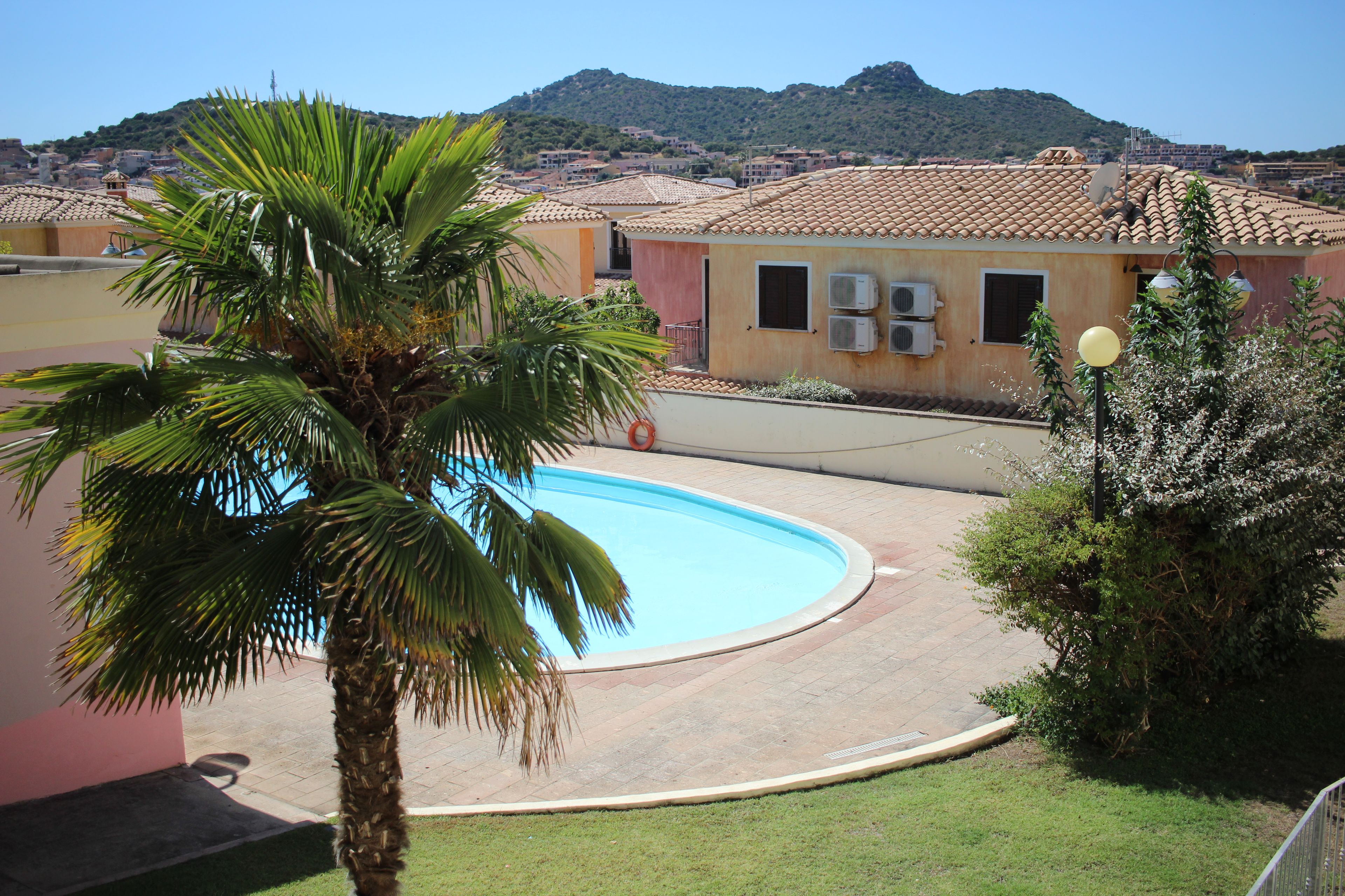 A residential area with a swimming pool, palm trees, and a view of a hilly landscape.