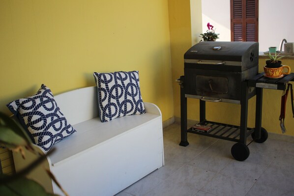 A white sofa with patterned cushions, a grill cart, and a small potted plant. - Villasimius, air conditioning and pool. CIN Code IT111105C2000Q2721 (Villasimius)