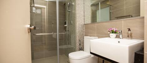 A modern bathroom with a glass-enclosed shower, a white toilet, and a sink with a mirror above.