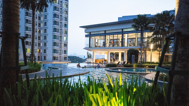 A modern hotel with a pool area, surrounded by palm trees and a high-rise building in the background.