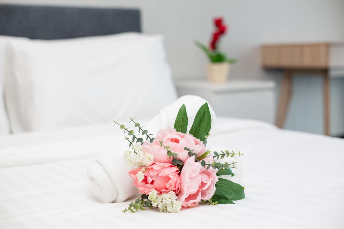 Un lit bien fait, agrémenté d’un arrangement floral sur la table de chevet.