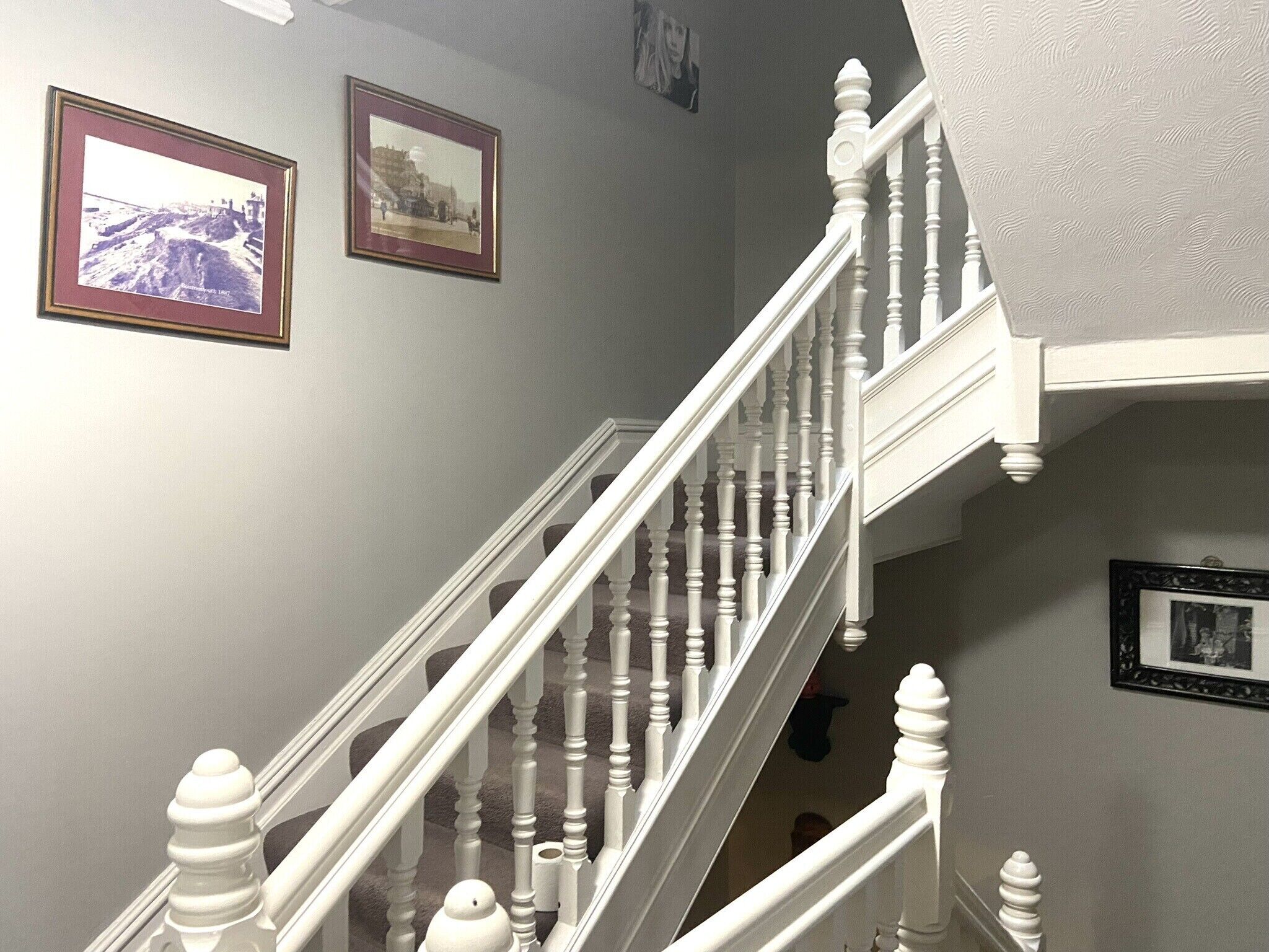 Una escalera con balaustres blancos y barandilla, que sube a un piso superior.